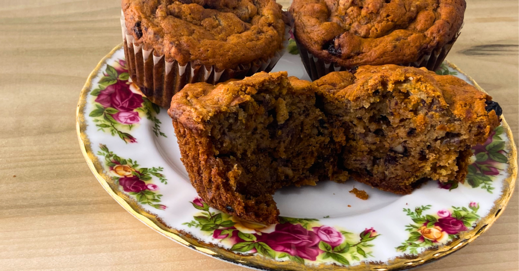 Three finished banana nut muffins on plate with one of them sliced to show delicious looking insides