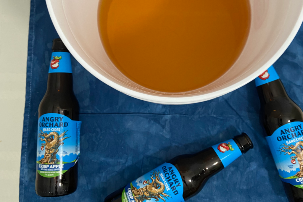 overhead photo of hard apple cider in a bucket and becoming flat while surrounded by empty hard apple cider bottles