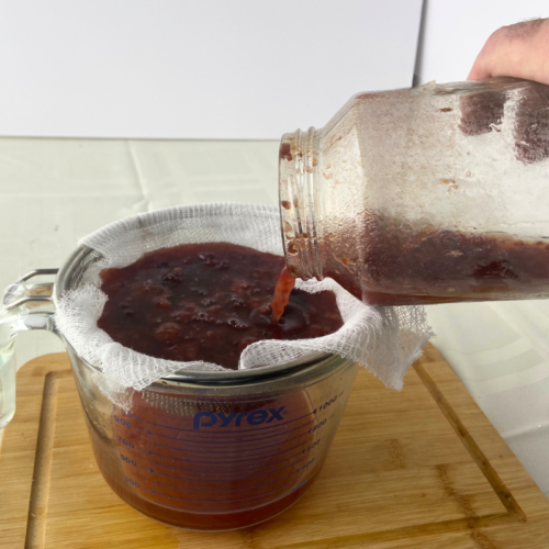 pouring a vinegar drink through a cheese cloth to strain fruit