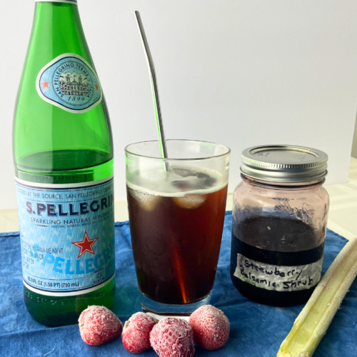 Strawberry rhubarb shrub in jar with sparkling water, fruit ingredients and a mixed shrub in glass with metal straw