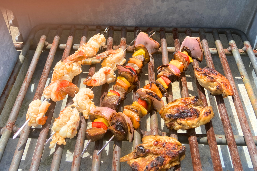 Food & Drink marinated jumbo shrimp on skewers, marinated beef shish kabobs, and marinated chicken thighs on a grill