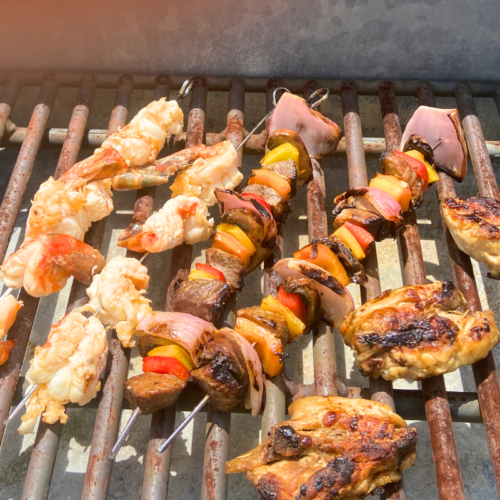 marinated jumbo shrimp on skewers, marinated beef shish kabobs, and marinated chicken thighs on a grill