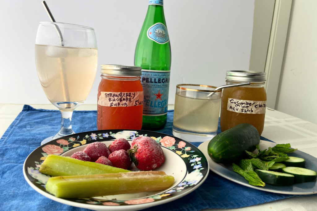 Jars of Strawberry Rhubarb and Blackberry Raspberry Shrubs with sparkling water diluted shrub mocktails and fruit ingredients.