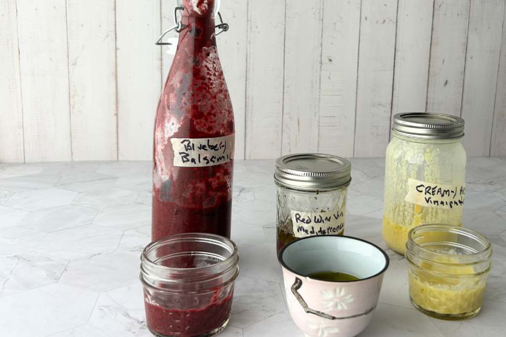 Bottle of blueberry balsamic vinaigrette and small jars of Red Wine vinegar Mediterranean vinaigrette and creamy ACV vinaigrette.