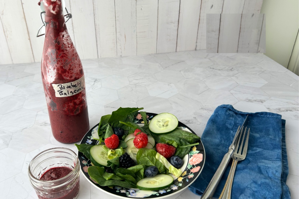 A bottle of blueberry balsamic vinaigrette with a cucumber and berry spinach salad and napkin and dining ware.