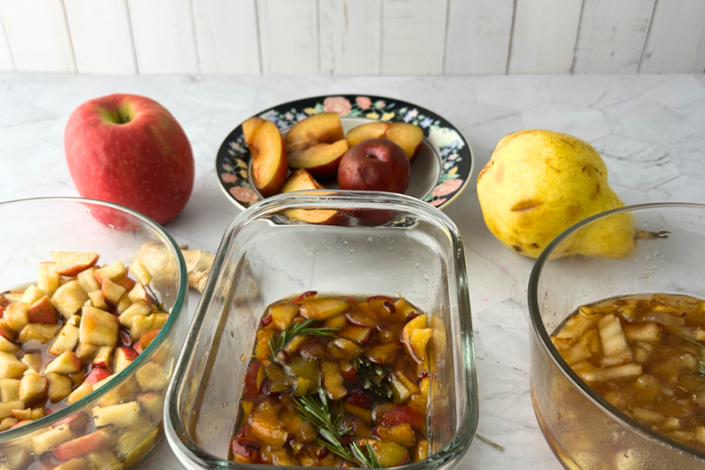 Apples, plums, and pear used in autumn shrub recipes turning to syrup in bowls with fresh fruit in background.
