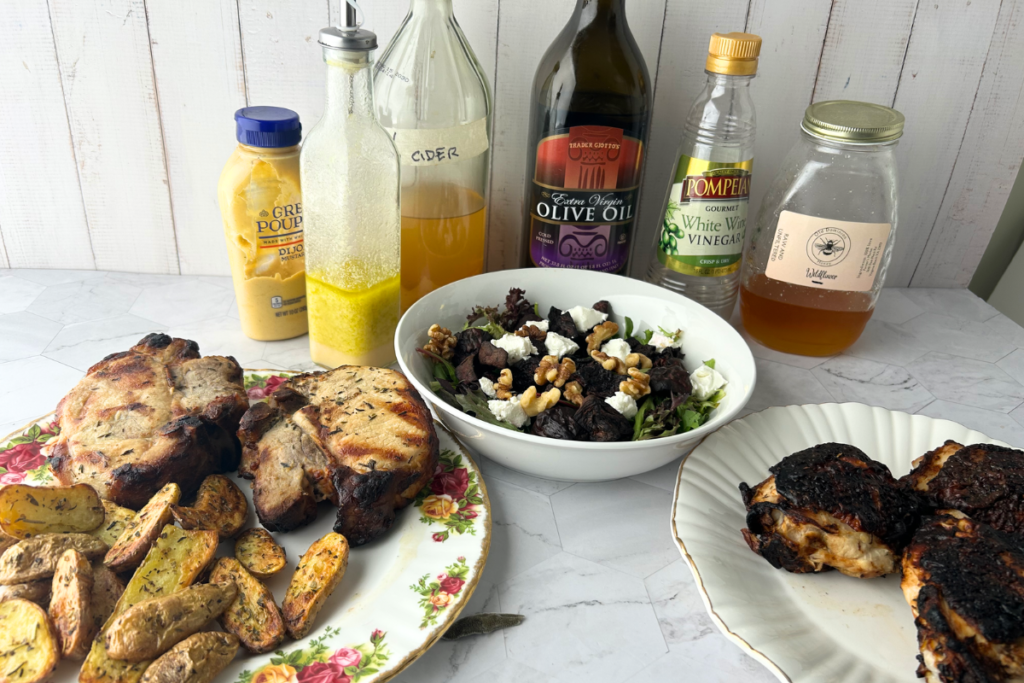 Prepared marinated grilled pork chops on plate with roasted potato fingerlings, roasted beet salad with greens, cheese, and walnuts, and marinated grilled chicken on a plate with autumn vinegar marinade ingredients in background.